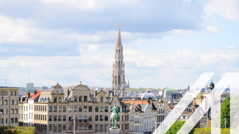 Stadtansicht von Brüssel mit einem historischen Turm im Zentrum, rund um die alten Häuser und das Reiterstandbild ist ein Park angelegt. Über das Bild wurde ein weißes Austria A gelegt.