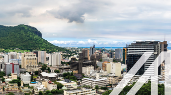 Blick auf die modernen Häuser von Port Louis, Mauritius. Links im Bild erhebt sich ein bewaldeter Hügel, in der ferne erkennt man das Meer.<br />
