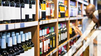 Pärchen vor Weinregal voller Flaschen bei der Auswahl einer Weinflasche im Lebensmittelgeschäft 