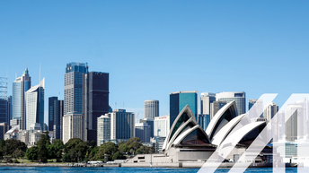 Stadtansicht von Sydney:  Blick vom Wasser auf die Skyline mit der berühmten Oper, umgeben von zahlreichen Wolkenkratzern. Über das Bild wurde ein weißes Austria A gelegt.