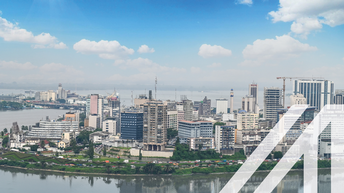 Stadtansicht von Abidjan unter blauem Himmel mit modernen Hochhäusern an einem begrünten Ufer