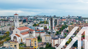 Stadtansicht von Pristina: Bunte Häuser und eine Kirche, im Hintergrund nebelverhangene Bergkette