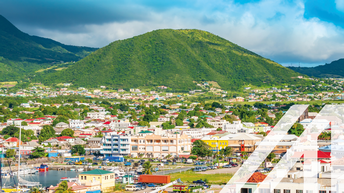 Ansicht von Basseterre: im Vordergrund Wasser und Hafen sowie kleine Stadtlandschaft, im Hintergrund begrünte Hügel unter wolkenverhangenem Himmel