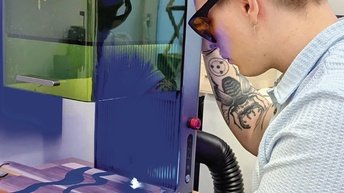 Rückenansicht einer Person mit Schutzbrille, die an einem 3D-Drucker steht