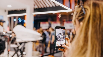 Eine junge Frau fotografiert mit ihrem Handy den Messestand der AUSSENWIRTSCHAFT AUSTRIA