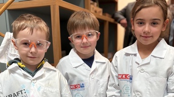 Kindergartenkinder in gebrandeten Labormänteln und Schutzbrille, die in die lächeln