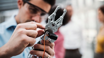 Person mit Schutzbrille bedient einen Roboterarm, Close-up
