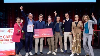 Mehrere Personen stehen nebeneinander auf einer Bühne. In der Mitte ist eine Person, die einen Scheck in Form eines Plakats mit dem Schriftzug € 20.000 in der Hand