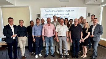 Vier Personen bei einer Urkundenübergabe in einem Veranstaltungsraum.