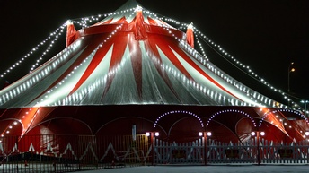 Außenaufnahme eines beleuchteten rot-weißen Zirkuszeltes bei Nacht