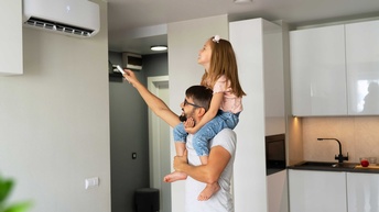 Ein Mann trägt ein Kind auf seinen Schultern, das mit einer Fernbedienung eine Klimaanlage einschaltet