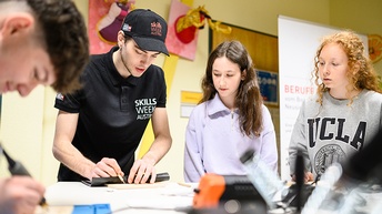 Vier Personen auf Tisch blickend, eine Person schneidet Folie