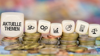 Würfel mit Schriftzug aktuelle Themen und unterschiedlichen Icons auf Münzen platziert