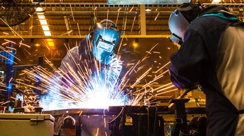 Zwei Personen in Schutzkleidung beim Schweißen, Funken sprühen.