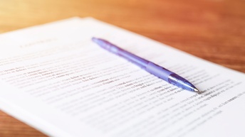 Nahaufnahme eines bedruckten Zettels, der auf einem Tisch liegt. Auf dem Zettel liegt ein Stift