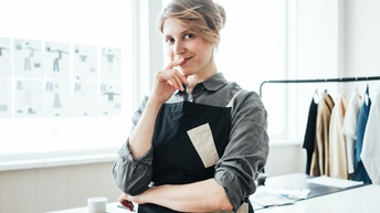 Schneider:in lächelnd in Atelier stehend