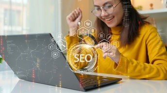 Eine Person sitzt an einem Tisch. Vor ihr ist ein aufgeklappter Laptop. Die Person hält eine Lupe über die Tastatur. Über dem Bild sind verschiedene Symbole in Kreisen und Sechsecken. In der Mitte steht im Kreis SEO