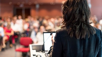 Rückansicht von einer vortragenden Person in einem vollen Konferenzraum