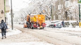 Ein Schneeräumungsfahrzeug räumt den Schnee auf den Straßen bei starkem Schneefall, auf den Gehwegen befinden sich Leute.