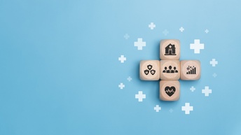 Auf hellblauem Hintergrund liegen vier Holzwürfel, die ein Kreuz bilden. Auf jedem Würfel ist ein anderes Symbol, zum Beispiel ein Krankenhaus oder ein Herz mit einer Frequenz darin