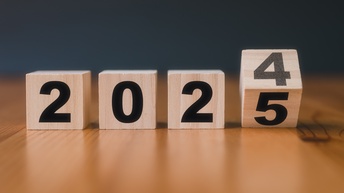 Vier Holzwürfel liegen auf einem dunklen Holztisch. Auf den Würfeln sind die Zahlen 2024 abgebildet, beim letzten Würfel geht die Zahl in die 5 über. Es wird der Jahreswechsel mit Symbolen dargestellt. <br />
