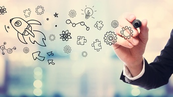 Hand in Businesskleidung zeichnet ein Ideenkonzept auf eine Glasscheibe, im Hintergrund zeigt sich ein Bokeh