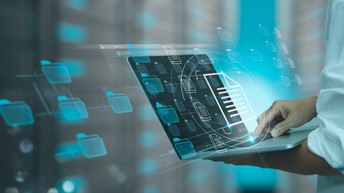 Seitliche Aufnahme einer Person, die einen Laptop hält. Auf dem Bildschirm sind mehrere Icons von Ordnern. Über der Tastatur ist das Icon eines Dokuments