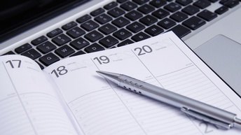 Detailansicht eines Kalenders, daraufliegend Kugelschreiber, im Hintergrund Computertastatur