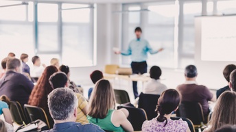 Vortragender vor einem gemischten Publikum von hinten in einem Konferenzsaal. 