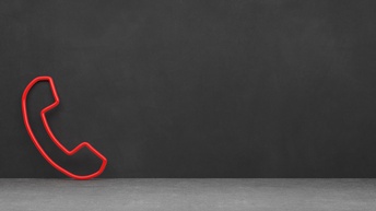 Rote Röhren in Form eines Telefonhörers an grauer Wand lehnend