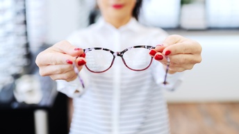 Person in Optikfachhandel bietet Brille zur Anprobe an