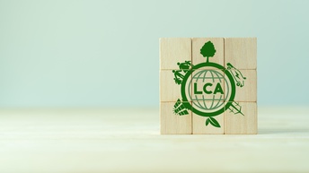 Neun Holzwürfel in Dreierreihen übereinander positioniert mit grünem Schriftzug LCA umrandet von Symbolen zur Nachhaltigkeit wie Windräder, Solaranlagen und Pflanzen.