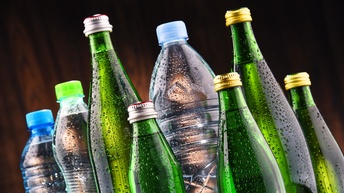 Nahaufnahme von verschiedenen Flaschen gefüllt mit Mineralwasser vor einem dunklen Hintergrund, Wassertropfen befinden sich gesprenkelt auf den Flaschen