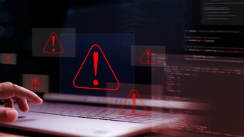 Eine Person hat ihre linke Hand bei der Tastatur eines aufgeklappten Laptops. Über der Tastatur sind sechs rote Dreiecke, in denen jeweils ein Rufzeichen ist