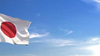 Die Flagge des Landes Japan weht an einem Mast angebracht im Wind. Im Hintergrund ist blauer Himmel mit vereinzelten Wolken zu sehen.