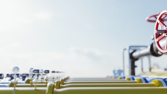 Mehrere gelbe Rohre im Ausschnitt , im Fokus rotes Rad zur Druckregulierung, unter blauem Himmel im Sonnenlicht