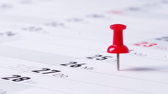 Termine sind mit bunten Stecknadeln auf einem Kalender markiert, Close-up