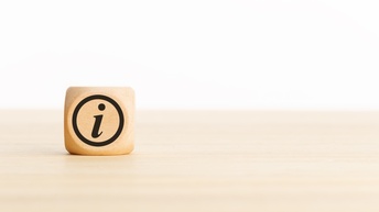Ein Holzwürfel mit dem Buchstaben i auf einem Holztisch vor hellem Hintergrund