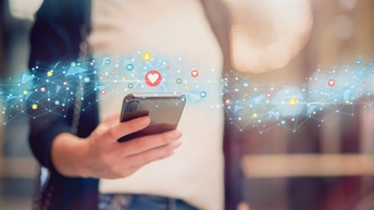 Detailansicht einer Hand, die Smartphone hält, darüberliegend Overlay von leuchtenden Linien und Social-Media-Icons