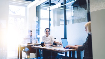 Mehrere Personen sitzen in Arbeitszimmer und verrichten Computerarbeit