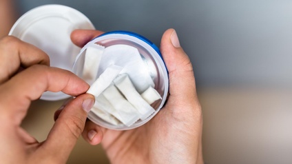 Die Hände einer Person halten eine kleine, geöffnete Dose, in der mehrere Nikotinbeutel sind