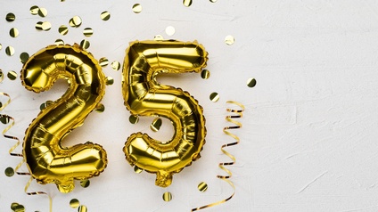 Auf hellem Hintergrund sind in der linken Bildhälfte Luftballons in denen Formen einer zwei und einer fünf. Daneben ist goldenes Konfetti
