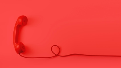 Roter Telefonhörer mit rotem Kabel eine Schlaufe bildend vor rotem Hintergrund