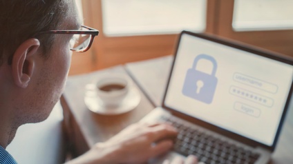 Person mit Brille im Fokus arbeitet an einem Laptop und versucht sich mit einem Passwort einzuloggen