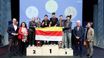 Die ersten drei Plätze in Mechatronik gehen nach Kärnten. Das Bild zeigt die Sieger auf dem Podest. Sie halten gemeinsam eine Kärnten-Fahne