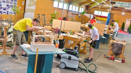 Halle mit jungen Leuten die an Werkbänken Tischlerarbeiten durchführen