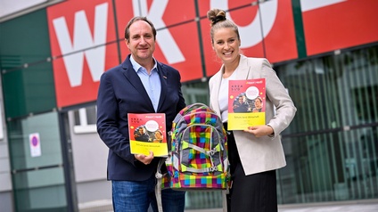 Herwig Draxler und Nika Basic halten gemeinsam einen Schulrucksack und jeder eine der neuen AREA-SÜD-Schulunterlagen