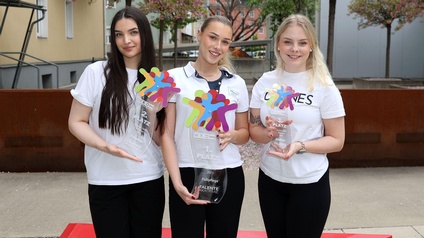 Die drei Erstplatzierten mit ihren Trophäen im Innenhof der Wirtschaftskammer Kärnten mit blühenden Bäumen im Hintergrund