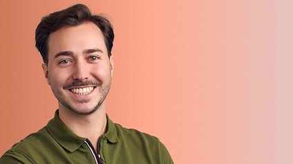 Georg Bertl lächelt in die Kamera vor orangem Hintergrund