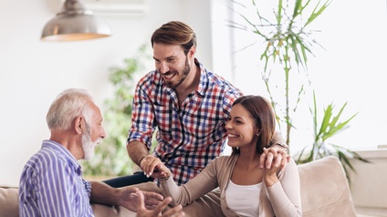 Freudige Unterhaltung eines Paares mit einer pensionierten Person auf einer Couch in einer Wohnzimmer-Atmosphäre